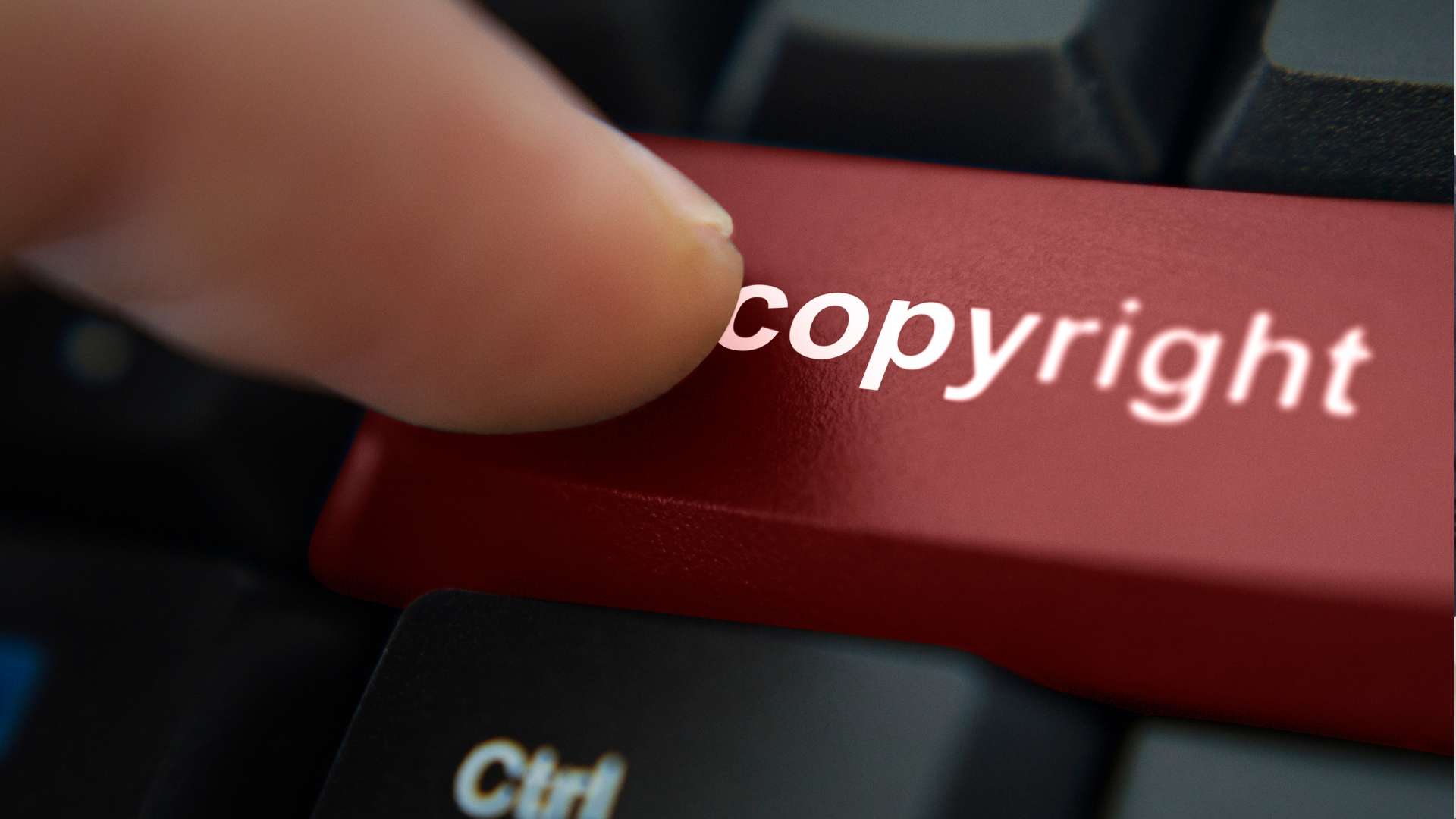 Finger pressing a red keyboard key labeled "copyright" next to a black "Ctrl" key.