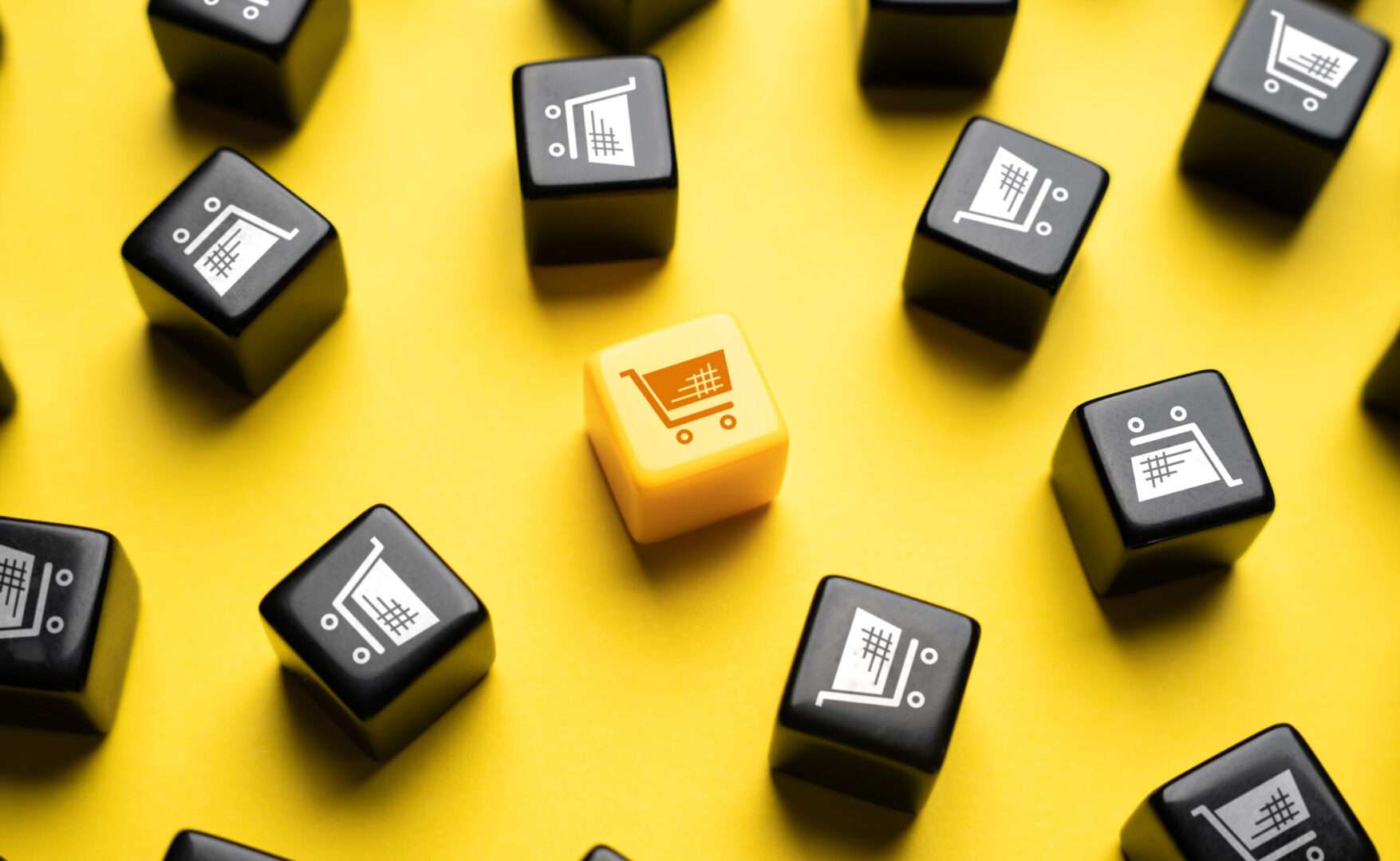 A single gold shopping cart dice standing out among black dice on a yellow background, representing the bold and strategic risk-taking behind the GameStop eBay unsolicited takeover bid and its lessons for small business owners navigating mergers and acquisitions.