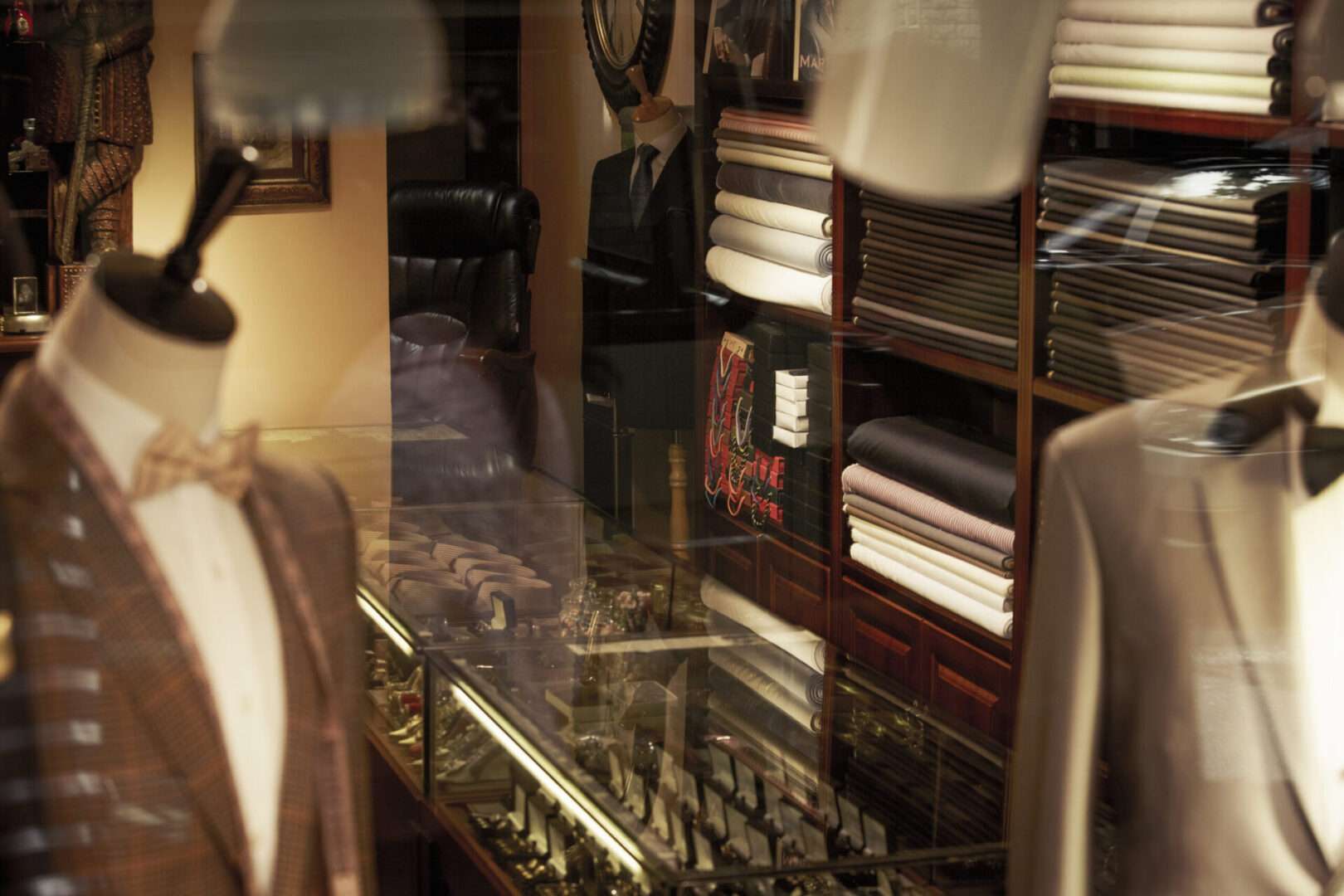 The interior of a traditional tailor shop featuring suit mannequins, stacked fabric bolts, and a glass display case, representing the craftsmanship and brand reputation that fashion businesses and small business owners must carefully protect.